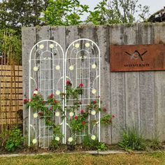 an iron garden trellis with flowers growing out of it and a sign on the fence