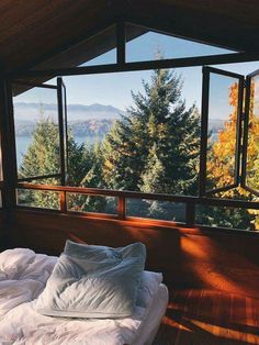 an unmade bed in front of a large window overlooking the trees and mountains outside