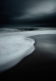 a black and white photo of the ocean with dark clouds in the sky above it