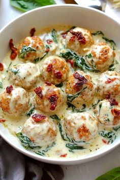 a white bowl filled with meatballs covered in cheese and spinach leaves on top of a table