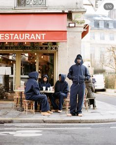 four people sitting at a table in front of a restaurant on the side of the street