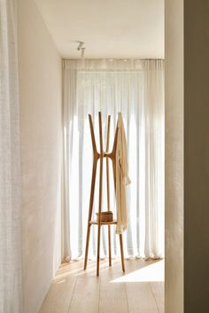 a coat rack in the corner of a room with white drapes on the windowsill