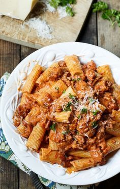 pasta with meat sauce and parmesan cheese in a white bowl on a wooden table