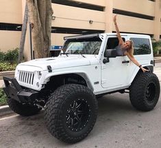 a woman standing on the hood of a white jeep with her arms in the air