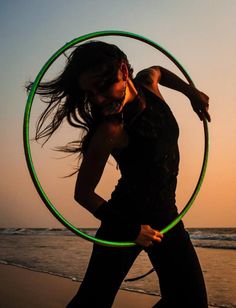 a woman is holding a hula hoop on the beach at sunset with her hair blowing in the wind