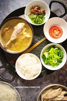 several bowls of food are arranged on a black tray with chopsticks, tomatoes and broccoli