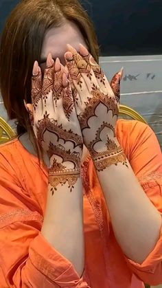 a woman covering her face with her hands while wearing henna designs on her hands