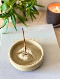 a small bowl with a stick sticking out of it's mouth on top of a table next to a candle