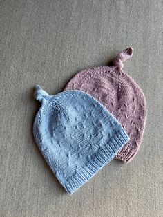 two knitted hats sitting next to each other on top of a gray tablecloth