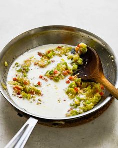 a pan filled with broccoli and other food on top of a table next to a wooden spoon