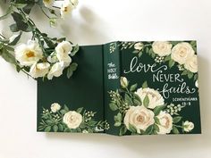 an open book with flowers on it and the words love never falls written in white