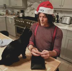 a man in a santa hat is petting a black cat on the kitchen counter