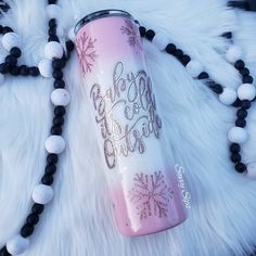 a pink and white snowflaked water bottle sitting on top of a black beaded necklace