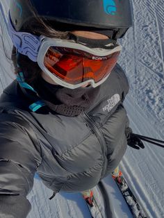 a person on skis in the snow wearing goggles and a black jacket with an orange lens