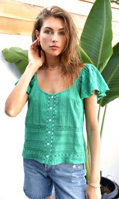 In an emerald shade, this relaxed top features a button front, lace detailing, and flutter sleeves. The lace decorations creates texture and dimension. The neckline lays in a unique way for an abstract silhouette. Flutter sleeve top Elastic sleeves Lace inserts Button front Self: 100% Cotton Length: 21 3/4" Chest: 18" Hand wash in cold water. Lay flat to dry. Low iron. Model is wearing a size small Style #: G234T6809 Casual Green Blouse With Ruffle Sleeves, Green Casual Flutter Sleeve Top, Casual Green Top With Flutter Sleeves, Bohemian Green Tops With Ruffles, Green Flutter Sleeve Blouse For Summer, Summer Ruffle Sleeve Tops With Buttons, Green Lace Top For Summer, Bohemian Green Blouse With Buttons, Green Bohemian Blouse With Buttons