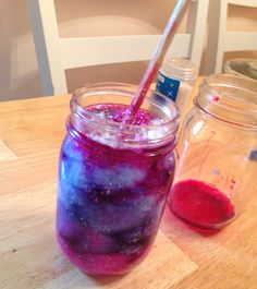 a glass filled with liquid sitting on top of a wooden table next to a jar