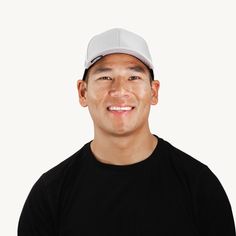 a man wearing a black shirt and a white hat smiles at the camera while standing in front of a white background