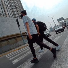 two people walking down the street with backpacks on their back and one person wearing a face mask