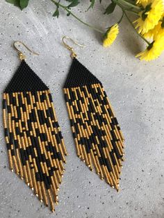 the black and gold earrings are next to yellow flowers on a gray surface with white speckles