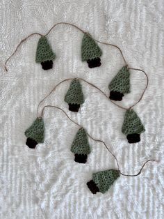 several crocheted christmas trees are hanging on a white sheet with twine needles