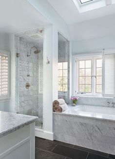 a bathroom with marble counter tops and white walls, along with a skylight above the bathtub