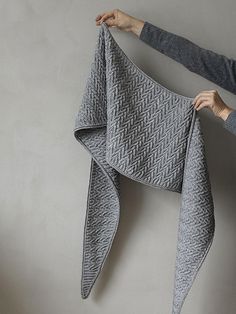 a woman holding up a gray knitted shawl in front of a grey wall