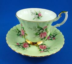 a tea cup and saucer with pink roses on green, gold trimmings