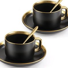 two black cups and saucers with gold rims, one has a spoon in it