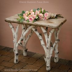 a wooden table with flowers on it and some branches sticking out of the top, sitting on a brick floor