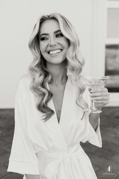 a woman with long hair holding a glass in her hand and smiling at the camera