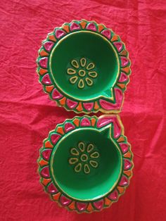 two green bowls with designs on them sitting on a red cloth covered tablecloth, next to each other