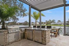 an outdoor kitchen with stainless steel appliances and grilling area next to the water, surrounded by palm trees