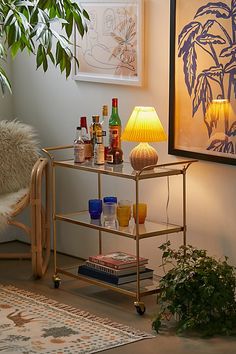 a small bar cart with drinks on it next to a lamp and potted plant