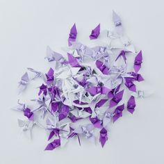 purple and white origami butterflies are scattered on a white surface with space for text