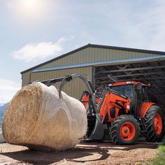 an orange tractor parked in front of a barn next to a bale of hay