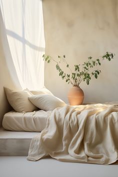 a plant in a vase sitting on top of a bed next to pillows and blankets