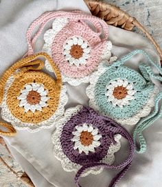 four crocheted purses sitting on top of a white cloth next to a basket