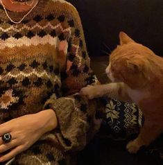 an orange and white cat sitting on top of a couch next to a woman wearing a sweater