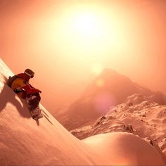 a snowboarder is going down the side of a snowy mountain at sun rise