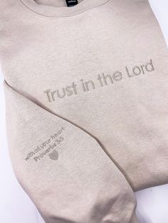 "This tan Trust in the Lord sweatshirt is inspiration to keep the faith! \"With all your heart\" embroidered on the sleeve adds a special touch and reminder for the wearer. Monochromatic embroidery lends it a muted, minimalist style while boldly communicating your faith. Makes a great gift for a Christian in your life, especially someone needing some encouragement. (and isn't that all of us!) All embroidery will be as pictured in the neutral color thread to match the shirt. About the sweatshirt: Christian Embroidered Sweatshirt, Christian Athletic Apparel, Christian Sweatshirt Designs, Christian Shirt Ideas, Monochromatic Embroidery, Minimalist Sweatshirt, Christian Embroidery, Christian Clothes, Christian Accessories