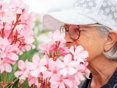 an elderly woman smelling pink flowers in a garden