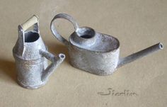 two metal watering cans sitting on top of a table