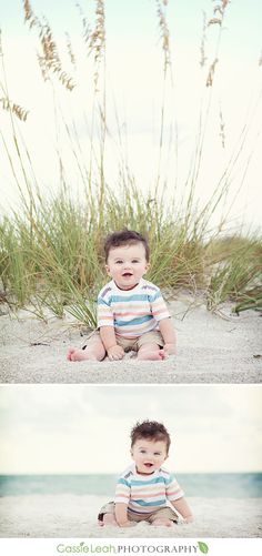 a baby sitting on the beach in front of tall grass and looking at the camera