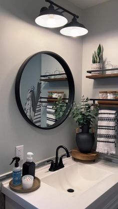 a bathroom sink sitting under a round mirror next to a shelf filled with toiletries