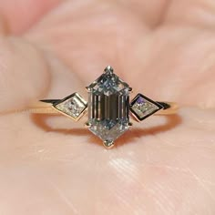 a close up of a person's hand holding a ring with an emerald stone