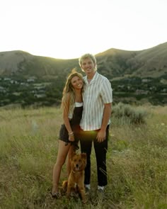 a man and woman standing next to a brown dog on top of a grass covered field