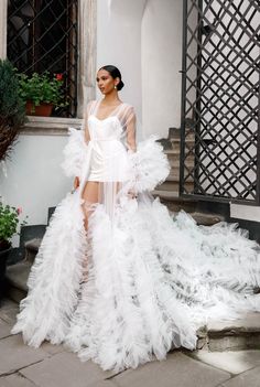 a woman in a white gown with feathers on the skirt is posing for a photo