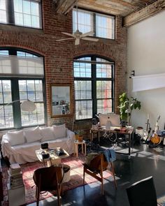 a living room filled with lots of furniture next to two large windows and a ceiling fan