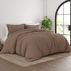 a bed with a brown comforter and pillows on top of it next to a potted plant