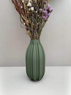 a green vase filled with lots of flowers on top of a white table next to a wall